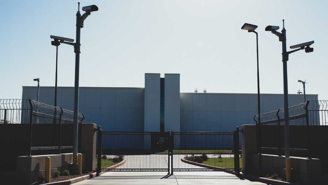 A high-security government facility with reinforced fencing, surveillance cameras, and a controlled access checkpoint, representing compliance with Homeland Security standards.
